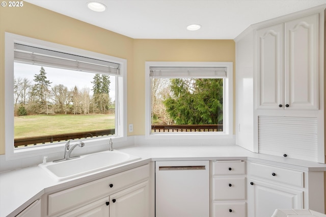 kitchen featuring dishwasher, light countertops, white cabinets, and a sink