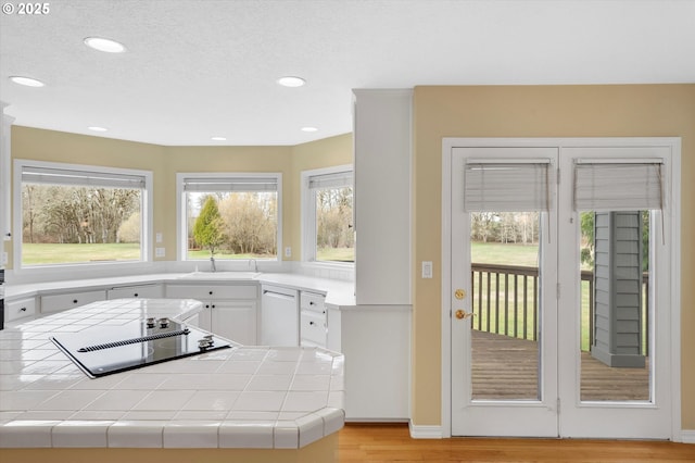 kitchen featuring light wood-type flooring, a sink, tile countertops, white cabinets, and white dishwasher