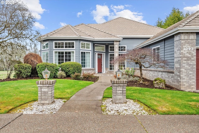 view of front of property with a front yard, a tiled roof, and brick siding