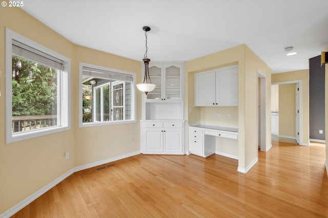 unfurnished dining area featuring visible vents, baseboards, built in desk, and light wood finished floors