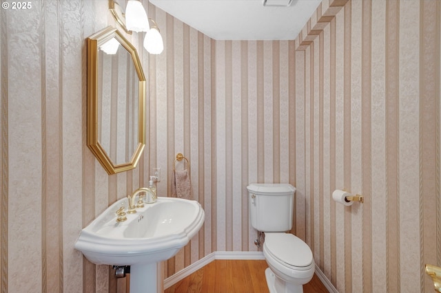 bathroom with wood finished floors, baseboards, wallpapered walls, a sink, and toilet