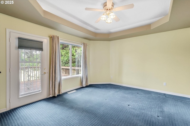 carpeted spare room featuring visible vents, baseboards, a tray ceiling, and a ceiling fan