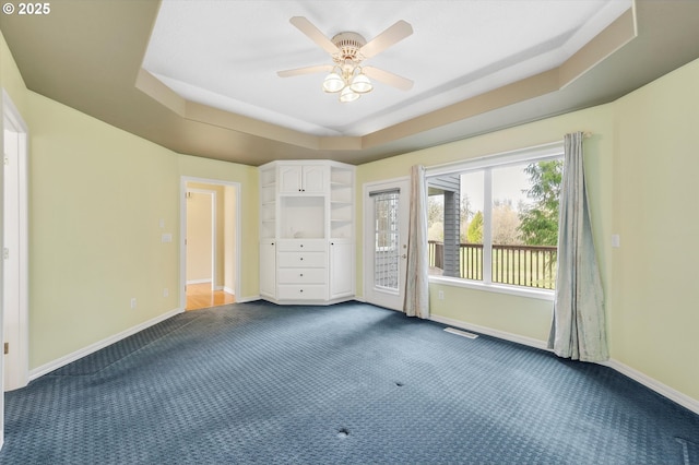 unfurnished bedroom with visible vents, a raised ceiling, dark carpet, baseboards, and access to exterior