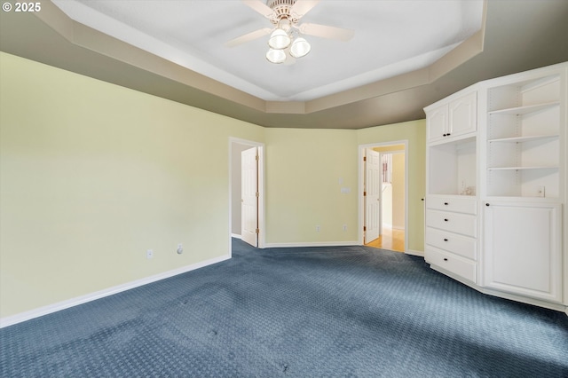 unfurnished bedroom featuring baseboards, a ceiling fan, a raised ceiling, and dark carpet