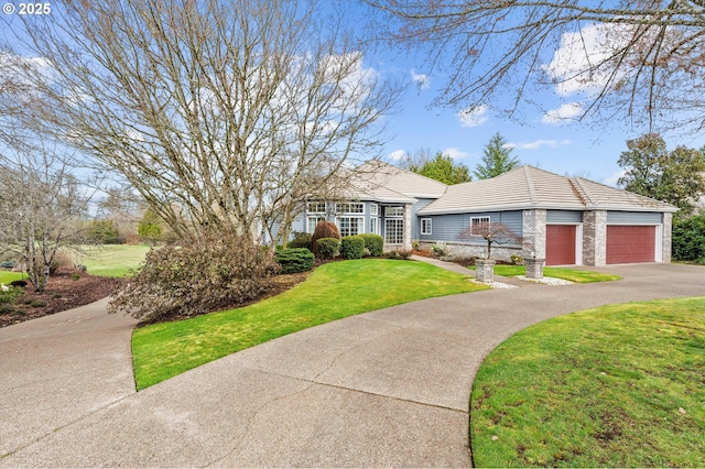 view of front facade with driveway, a front lawn, stone siding, an attached garage, and a tiled roof