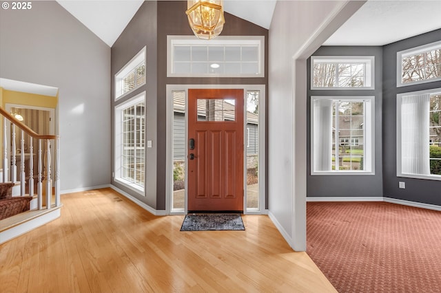 entrance foyer with stairway, high vaulted ceiling, baseboards, and wood finished floors