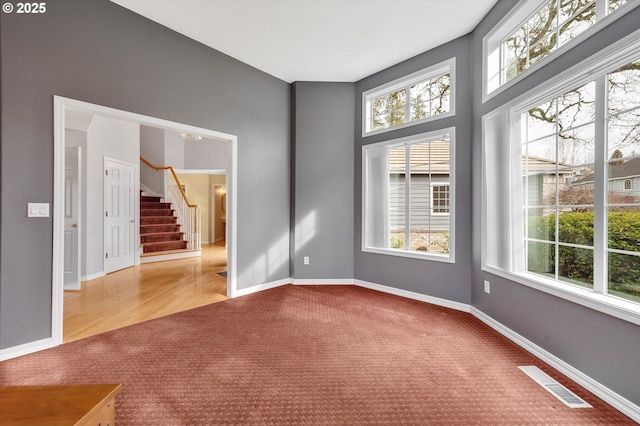 unfurnished room featuring a wealth of natural light, visible vents, carpet floors, and stairway