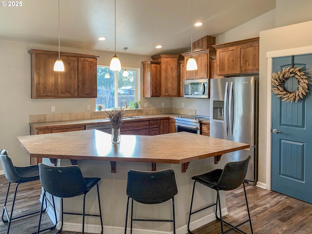 kitchen with pendant lighting, sink, appliances with stainless steel finishes, a kitchen island, and dark hardwood / wood-style flooring