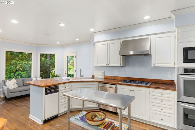 3925 SW Humphrey Blvd, Portland, OR 97221 - kitchen featuring stainless steel appliances, wall chimney range hood, a peninsula, crown molding, and white cabinets