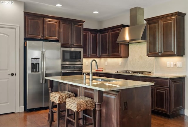 kitchen featuring appliances with stainless steel finishes, wall chimney range hood, a sink, dark wood-type flooring, and dark brown cabinets