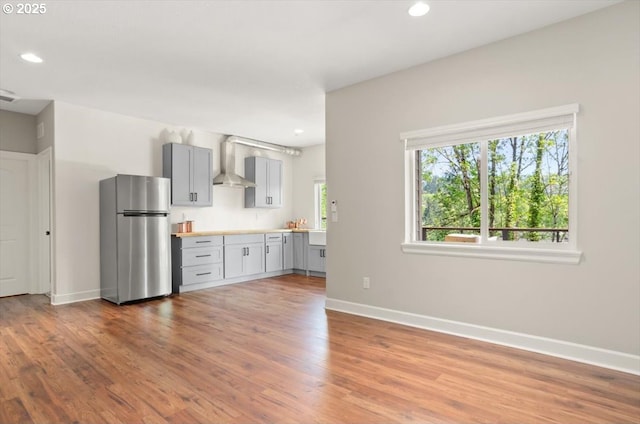 kitchen featuring freestanding refrigerator, wall chimney exhaust hood, gray cabinetry, light countertops, and recessed lighting