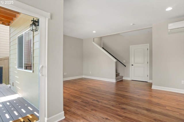 unfurnished living room featuring wood finished floors, stairway, an AC wall unit, baseboards, and recessed lighting