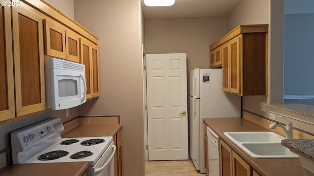 kitchen with a sink, light wood-style flooring, brown cabinets, and white appliances