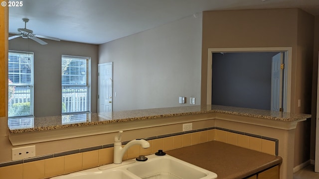 interior space with a ceiling fan, light stone counters, and a sink
