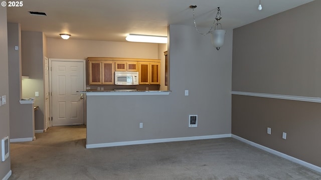 kitchen with visible vents, light carpet, baseboards, white microwave, and brown cabinets
