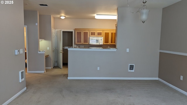 kitchen featuring visible vents, brown cabinets, baseboards, white microwave, and light carpet