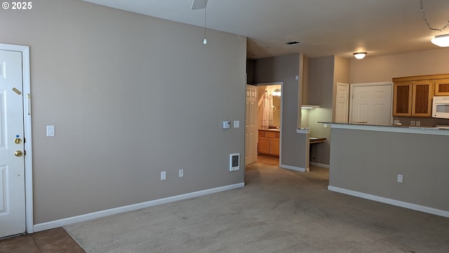 kitchen featuring baseboards, ceiling fan, white microwave, and brown cabinetry
