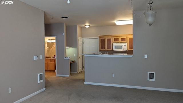 kitchen featuring visible vents, baseboards, white microwave, light colored carpet, and brown cabinets
