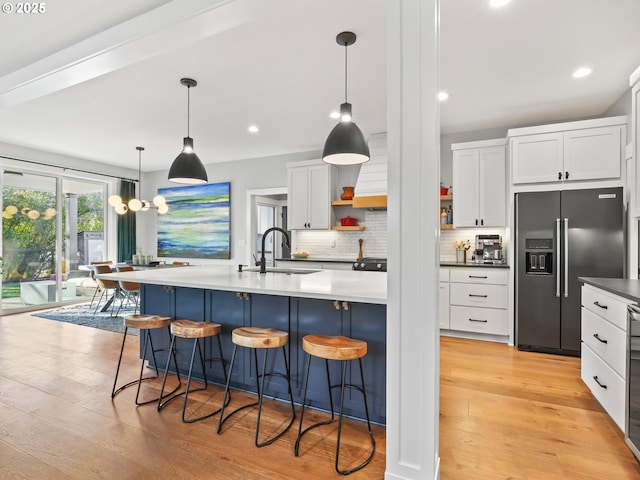 kitchen featuring high end black refrigerator, sink, white cabinets, a kitchen breakfast bar, and hanging light fixtures