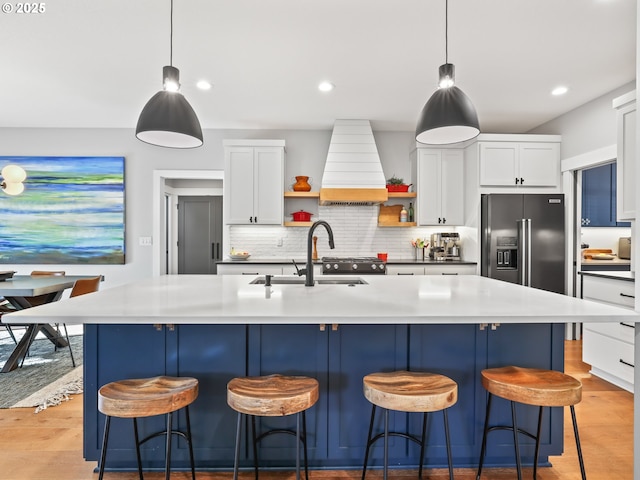 kitchen featuring custom exhaust hood, white cabinetry, a kitchen island with sink, and pendant lighting