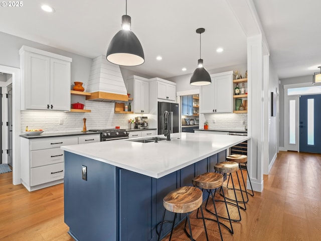 kitchen with premium range hood, an island with sink, hanging light fixtures, and white cabinets