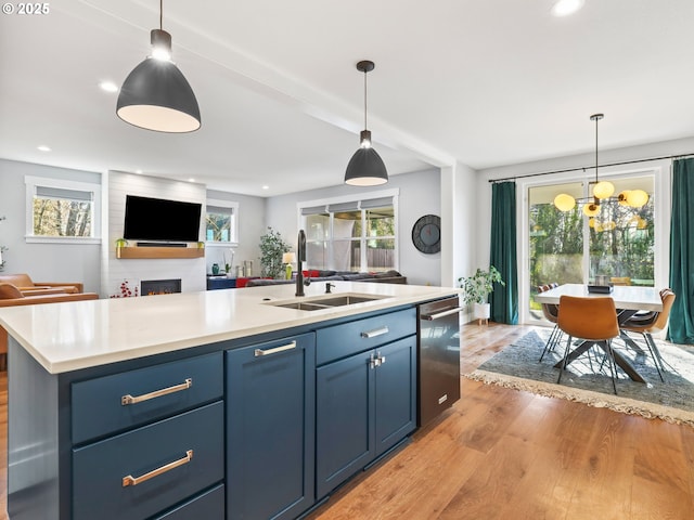 kitchen featuring pendant lighting, sink, a kitchen island with sink, blue cabinets, and light wood-type flooring