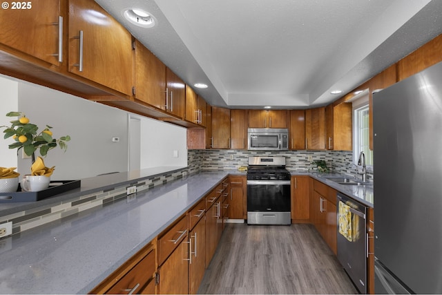 kitchen with brown cabinets, a sink, wood finished floors, stainless steel appliances, and a raised ceiling