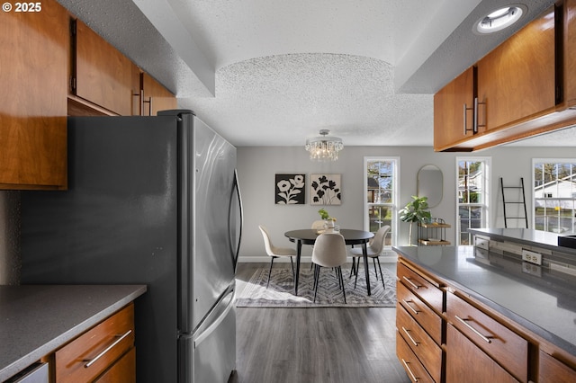 kitchen featuring brown cabinetry, a textured ceiling, freestanding refrigerator, and dark wood-type flooring