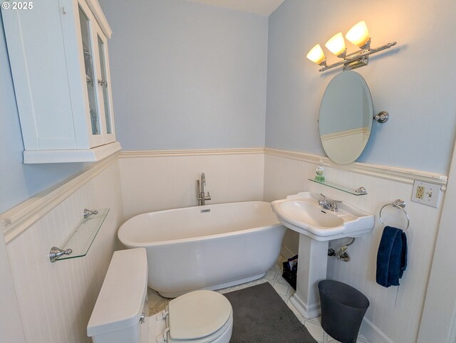 full bathroom with wainscoting, a soaking tub, and toilet