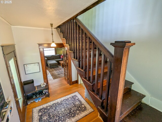 stairs featuring wood finished floors and ornamental molding