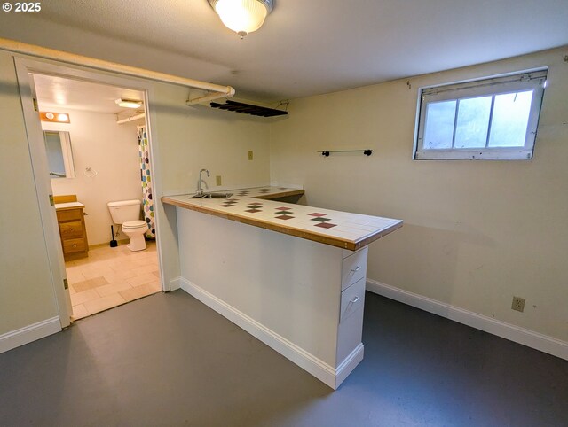 kitchen featuring a peninsula, tile counters, a sink, finished concrete floors, and baseboards