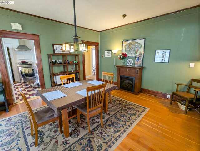 dining space featuring a fireplace, light wood-style flooring, crown molding, a chandelier, and baseboards