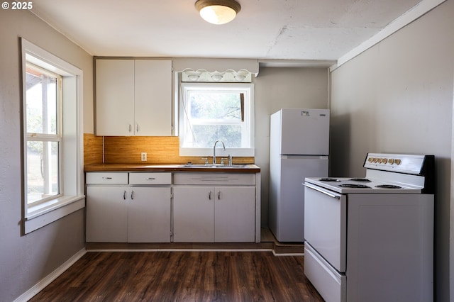 kitchen with dark wood finished floors, tasteful backsplash, dark countertops, a sink, and white appliances