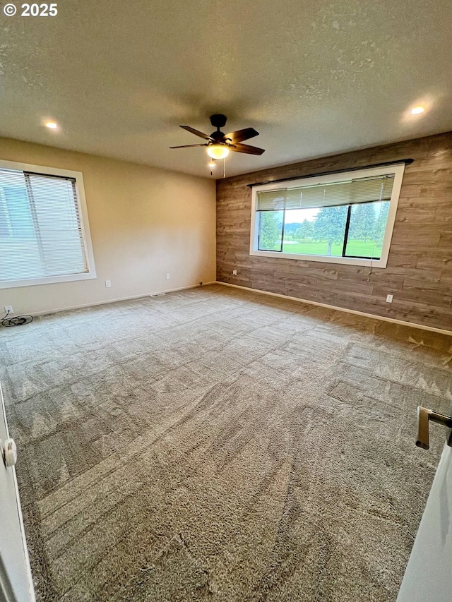 empty room with wood walls, a textured ceiling, ceiling fan, carpet flooring, and recessed lighting