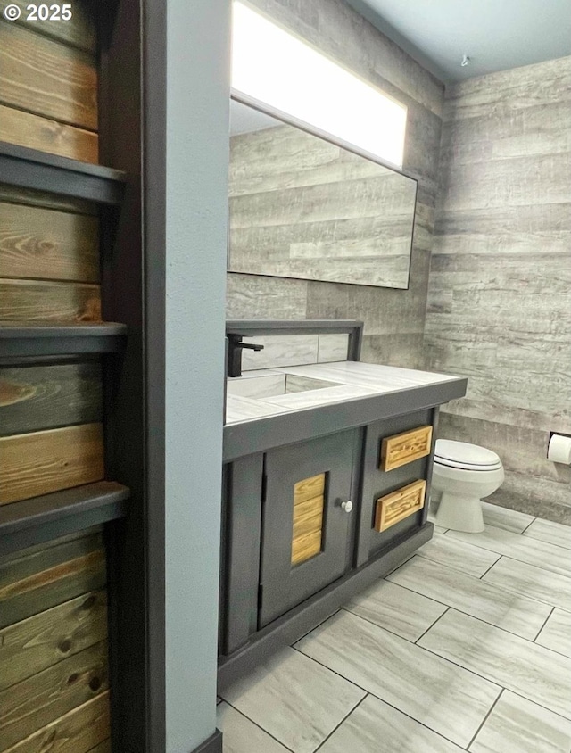 bathroom featuring wood walls, toilet, and vanity