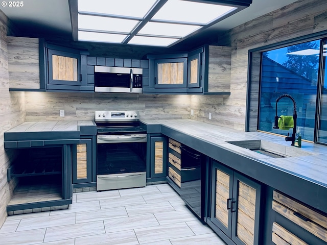 kitchen with appliances with stainless steel finishes, a sink, tile counters, and glass insert cabinets
