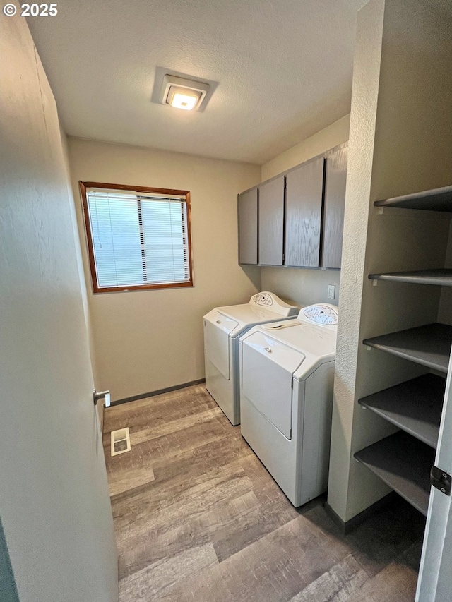 clothes washing area featuring washing machine and clothes dryer, cabinet space, and light wood-type flooring