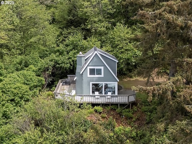 7975 NW Logan Rd, Lincoln City, OR 97367 - rear view of house with a wooden deck, a wooded view, and a chimney