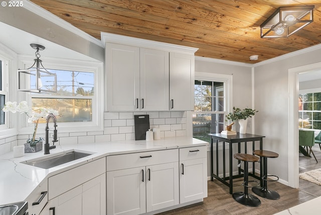 kitchen featuring sink, white cabinetry, hanging light fixtures, wooden ceiling, and ornamental molding