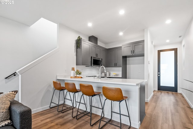 kitchen featuring sink, gray cabinets, a breakfast bar area, light hardwood / wood-style floors, and kitchen peninsula