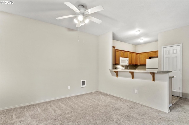 kitchen with a breakfast bar, light colored carpet, ceiling fan, kitchen peninsula, and white appliances