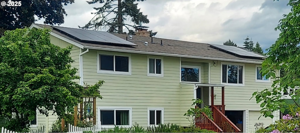 rear view of house featuring a garage, a chimney, and solar panels
