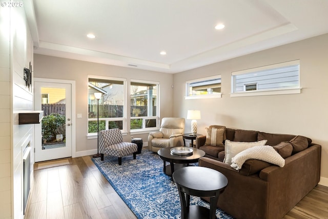 living area with baseboards, a tray ceiling, wood finished floors, and recessed lighting