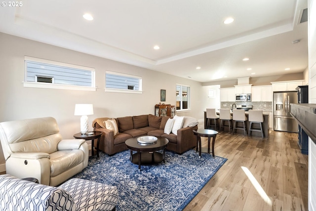 living room with light wood-style flooring, a tray ceiling, and recessed lighting