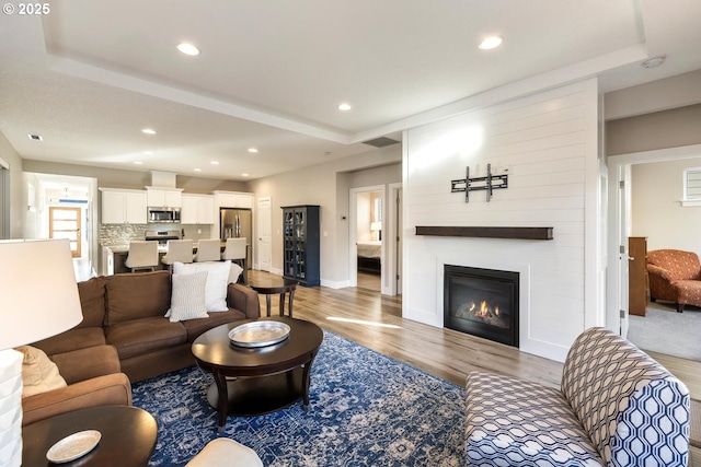 living area featuring recessed lighting, a fireplace, wood finished floors, visible vents, and a raised ceiling