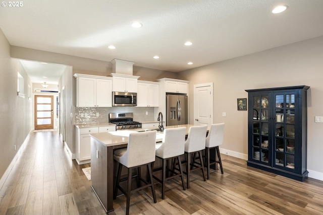 kitchen with white cabinets, a center island with sink, stainless steel appliances, and wood finished floors