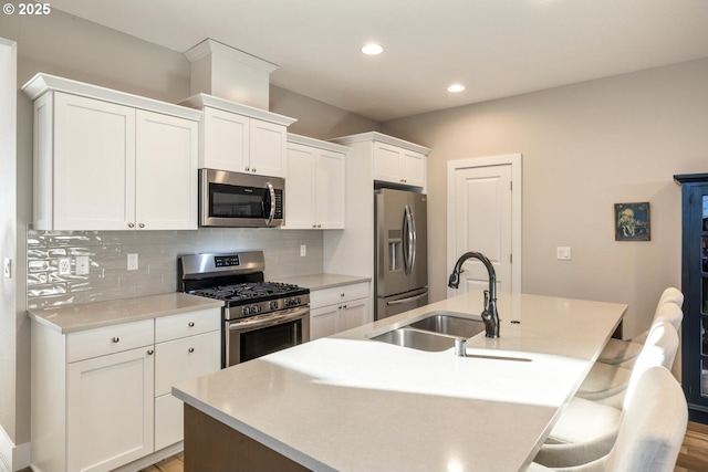 kitchen with a center island with sink, stainless steel appliances, decorative backsplash, white cabinets, and a sink