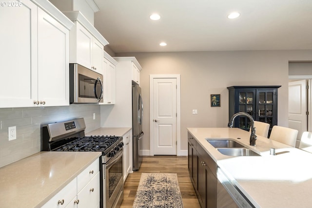 kitchen featuring light wood finished floors, light countertops, backsplash, appliances with stainless steel finishes, and a sink