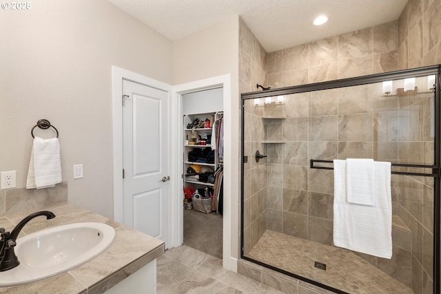 bathroom with a textured ceiling, a spacious closet, a shower stall, and vanity