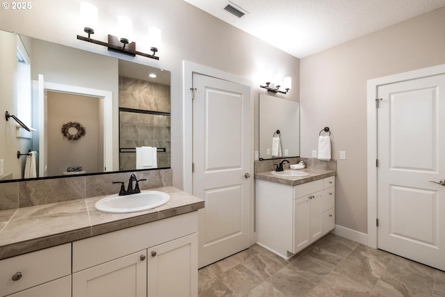 bathroom with a stall shower, visible vents, two vanities, and a sink